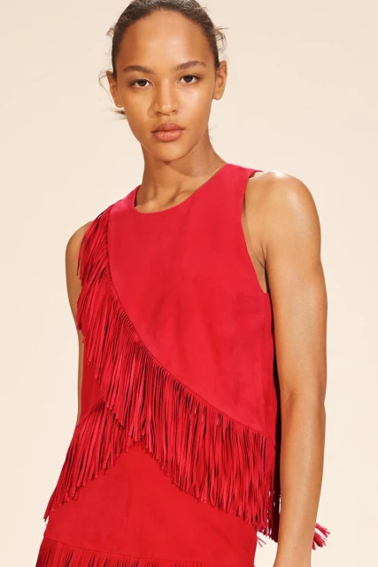 Close-up of a fashion model showcasing a sleeveless red top with fringe detail, against a neutral backdrop in a studio setting.