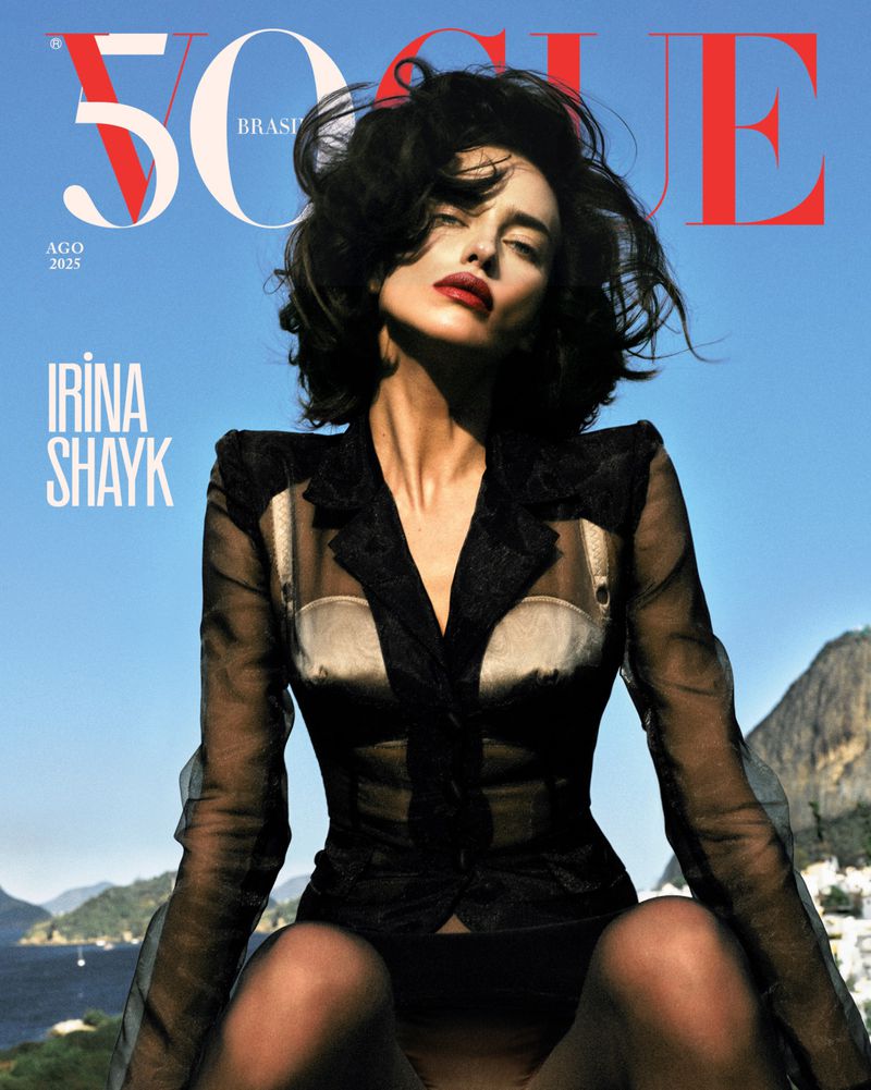 Vogue Brasil cover featuring Irina Shayk in a sheer black outfit against a backdrop of blue sky, mountains, and coastal buildings.