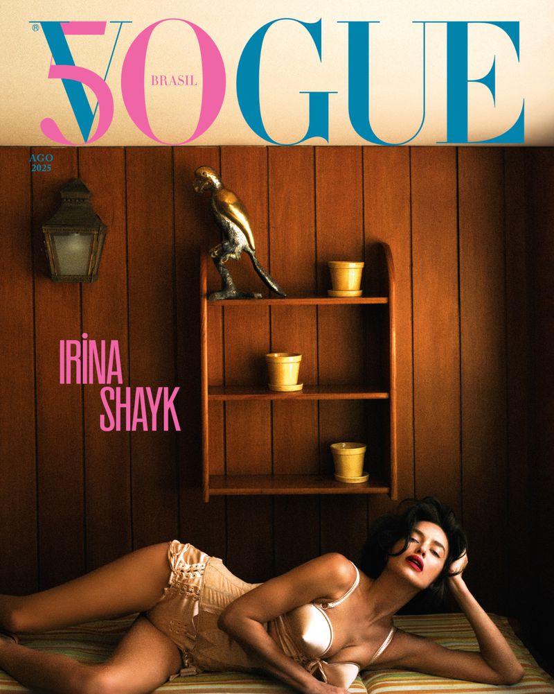 Irina Shayk lying down in lingerie for Vogue Brasil cover. She rests on a striped surface in front of wood-paneled wall.