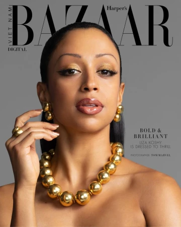 Close-up portrait of Liza Koshy, face forward, wearing golden jewellery against a grey backdrop for Harper's Bazaar Vietnam.