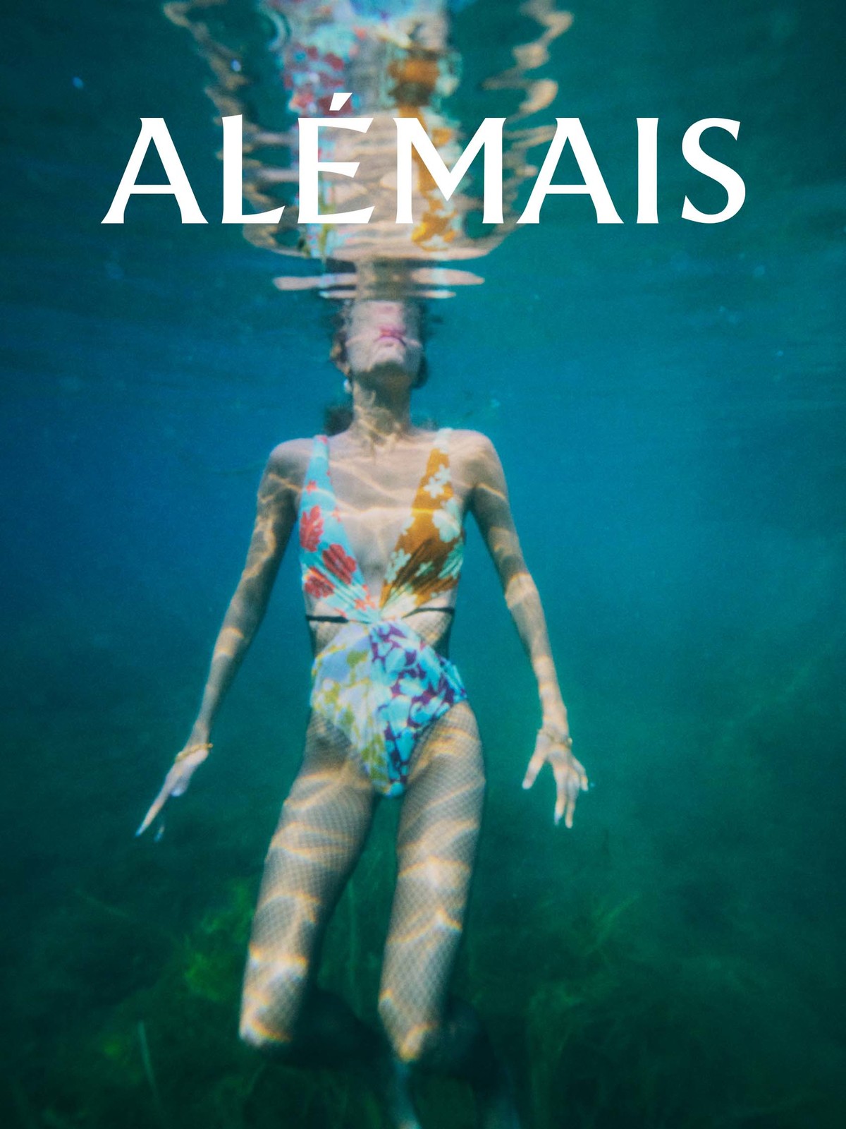 Woman in a floral swimsuit underwater in a pool or ocean with the brand name, Alemais, at the top of the image.