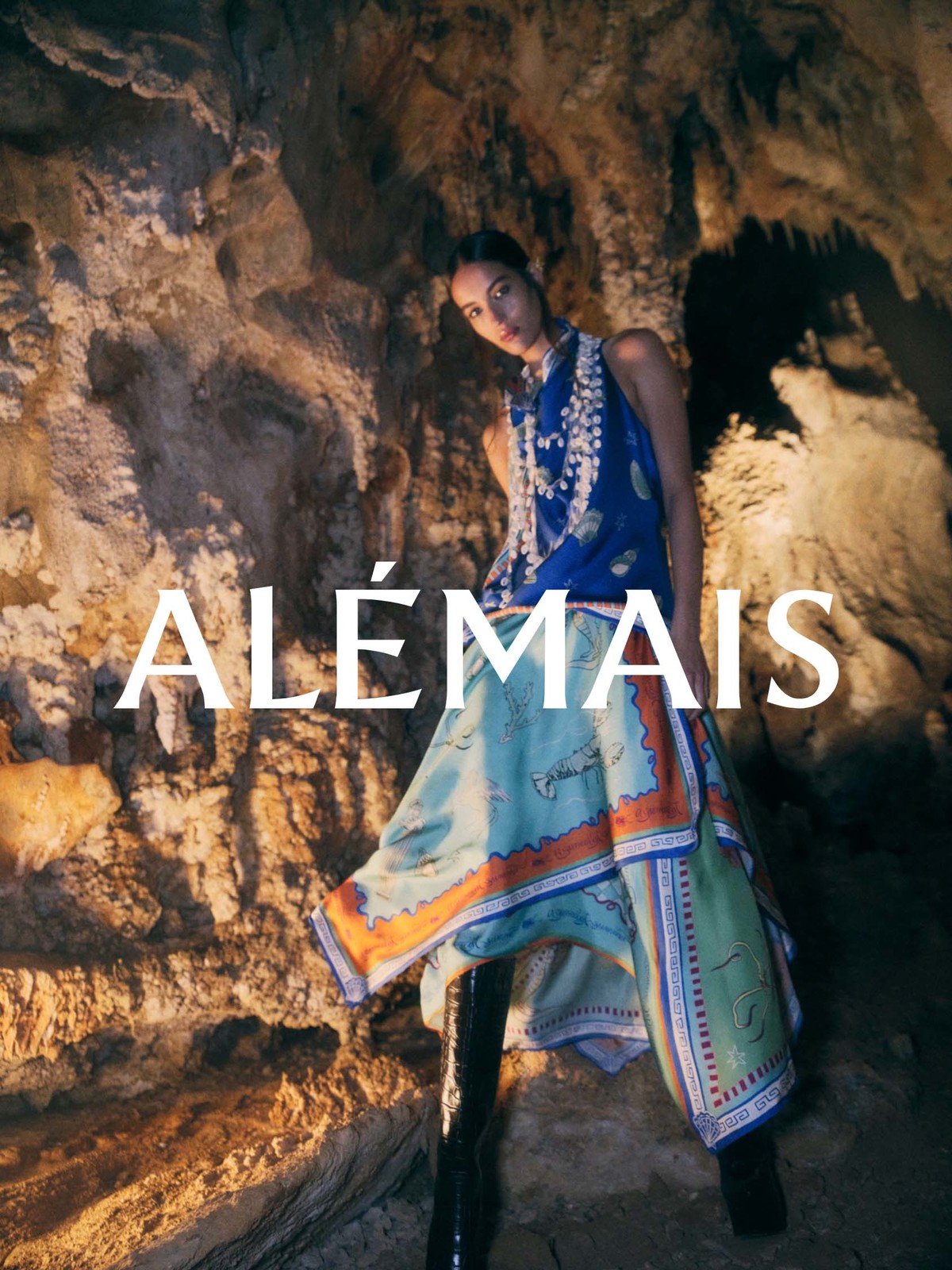 Model standing inside a natural stone cave wearing a patterned blue top and a printed skirt for Alemais Deep Sea Dreaming campaign.