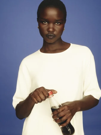 Portrait of a dark-skinned adult woman opening a soda bottle against a blue background in a close-up studio shot.