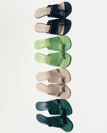 Arrangement of four pairs of leather toe-ring sandals in shades of dark blue, green, beige, and dark green on a white backdrop.