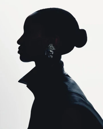Profile silhouette of a woman with a sleek bun wearing a collared jacket and a reflective statement earring against a white background.