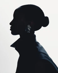 Profile silhouette of a woman with a sleek bun wearing a collared jacket and a reflective statement earring against a white background.