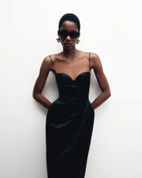 Model wearing a black slip dress and dark sunglasses against a white background for Magda Butrym