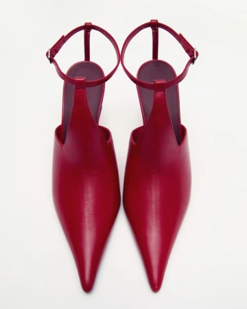 A pair of pointed-toe red leather ankle-strap heels viewed from directly above against a seamless white background.