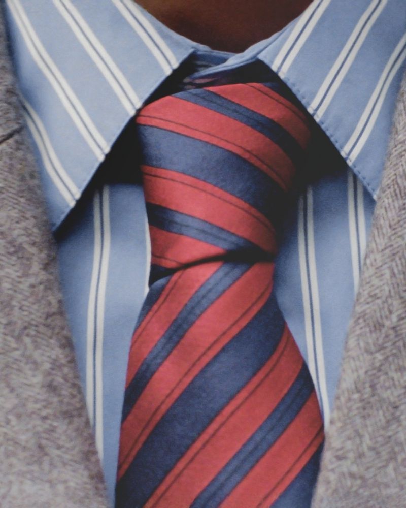 Close-up of a red and blue striped necktie knotted against a blue pinstripe dress shirt, showcasing formal wear and attention to detail.