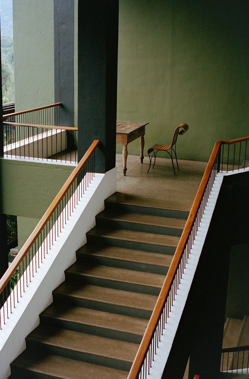 Indoor staircase and landing area features a wooden table and chair, a minimalist design with olive green wall paint.