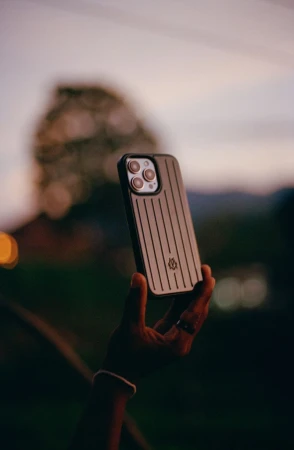 Hand holding an iPhone with a striped case against a blurred background of greenery, evoking a sense of technology in nature.