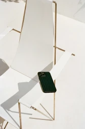 A dark green ribbed smartphone case rests on a white canvas and metal lounge chair outdoors in bright sunlight.