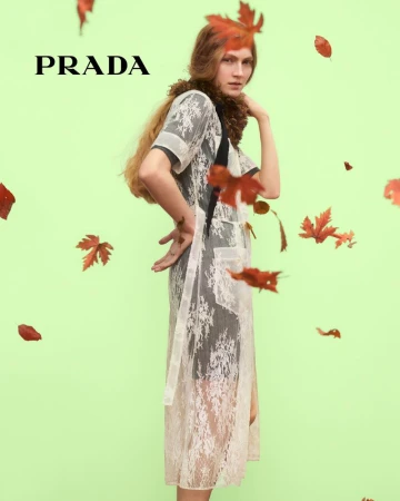 A woman in a lace dress poses in a studio with falling leaves and the Prada logo, creating a fashion-forward and seasonal visual.