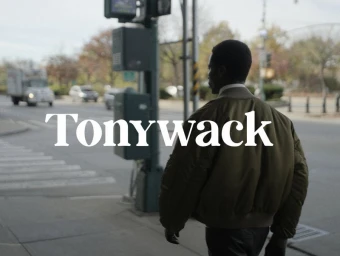 Man walking on a city street wearing a green bomber jacket, with Tonywack typography overlaid