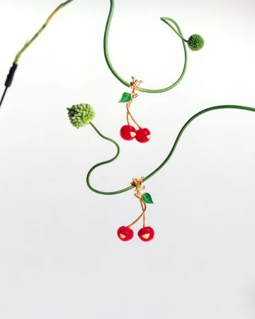Two cherry pendants hang from green vines on a white background, showcasing a playful and whimsical design in a minimalist composition.