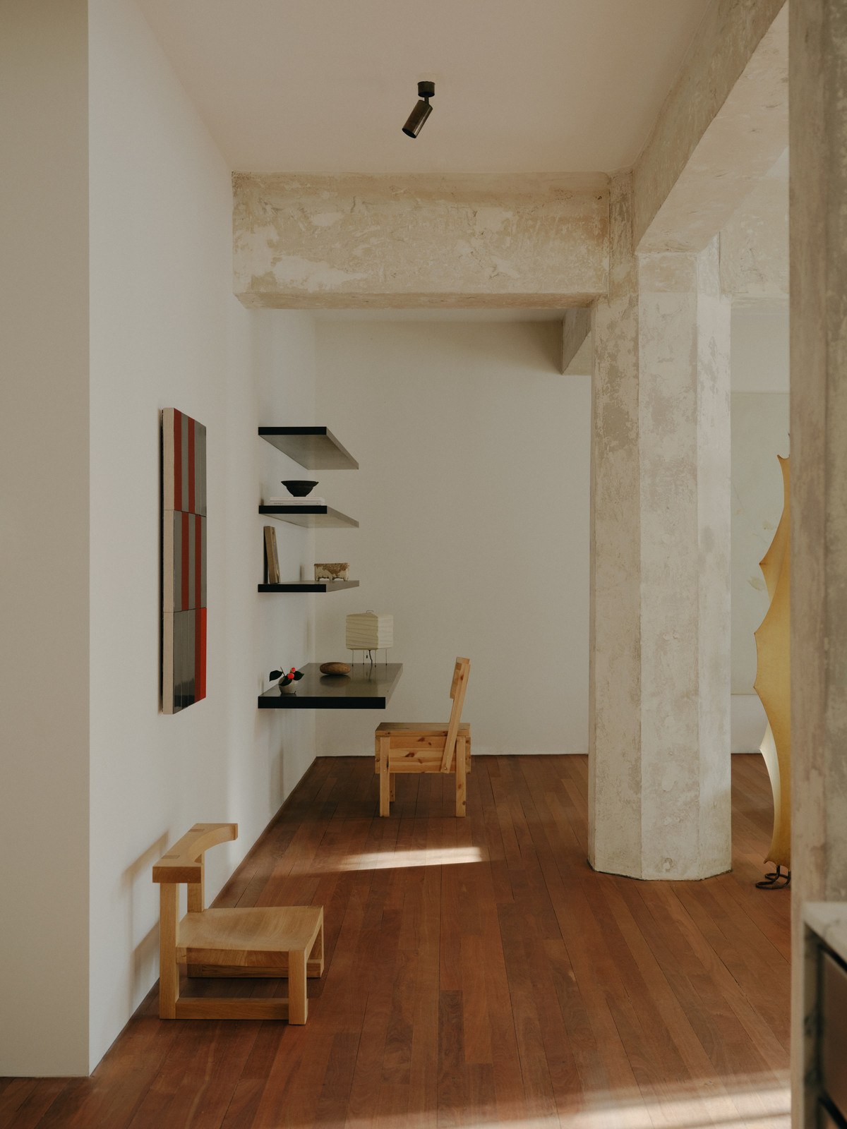 Minimalist interior with modern decor: wooden chairs, hardwood floor, abstract art, and floating shelves against a white wall.