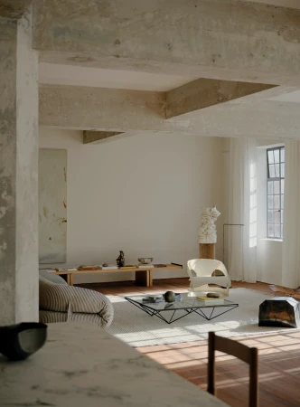 Sunlit living room interior with modern furniture, including a glass coffee table, a minimalist sofa, and a sculptural art piece.