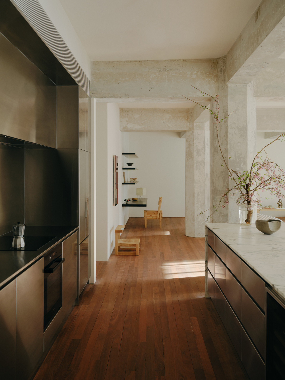 Modern kitchen and hallway in minimalist style. Features stainless steel kitchen units, wooden floor, and neutral-toned walls and ceiling.