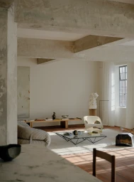 Minimalist living room interior featuring concrete beams, modern furniture, low glass coffee table, and soft natural lighting