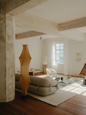 Minimalist living room interior with a low striped sofa, sculptural floor lamp, and large window with white curtains.