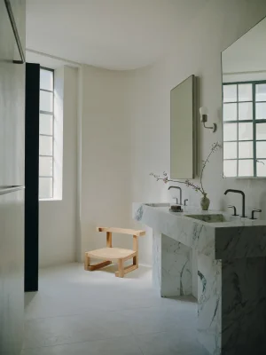 Minimalist bathroom interior with a white marble double vanity, wooden stool, and large grid windows casting soft natural light