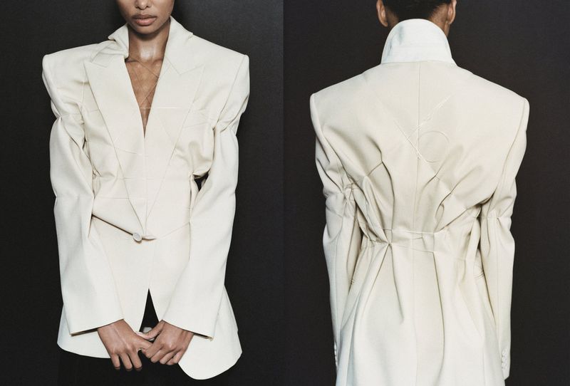 Two angles of a person modeling a cream-colored blazer with puffy sleeves against a dark backdrop in a studio fashion shot.