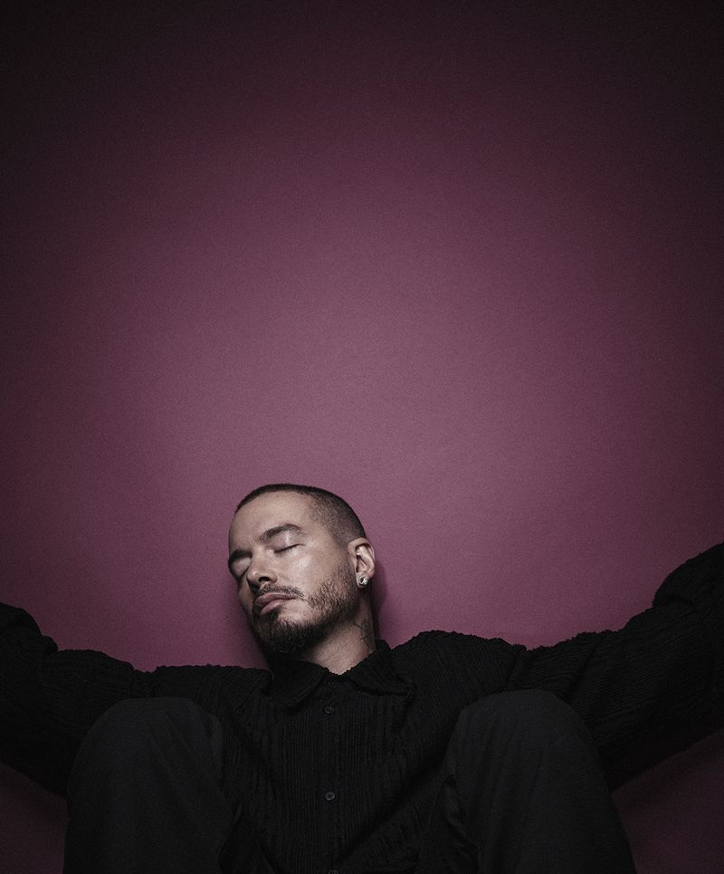 Portrait of a man with closed eyes in a black button-down shirt, posing against a pink-purple gradient background with diffused lighting.