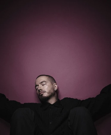 Portrait of a man with closed eyes in a black button-down shirt, posing against a pink-purple gradient background with diffused lighting.