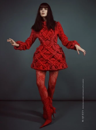 Brunette woman in red knit dress and matching tights and boots poses against a gray background in a studio fashion shot.