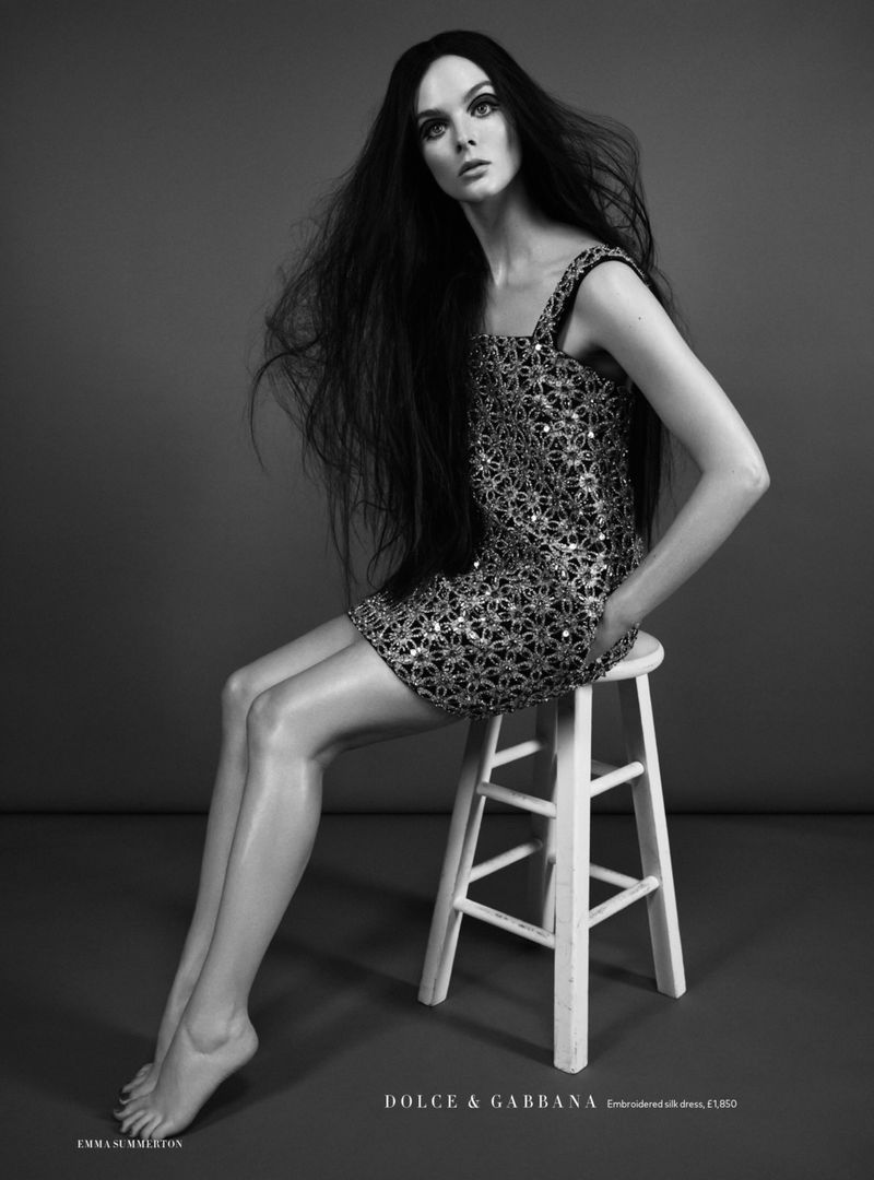 Model Aylah Peterson seated on a white wooden stool wearing a sequined mini dress against a studio backdrop.
