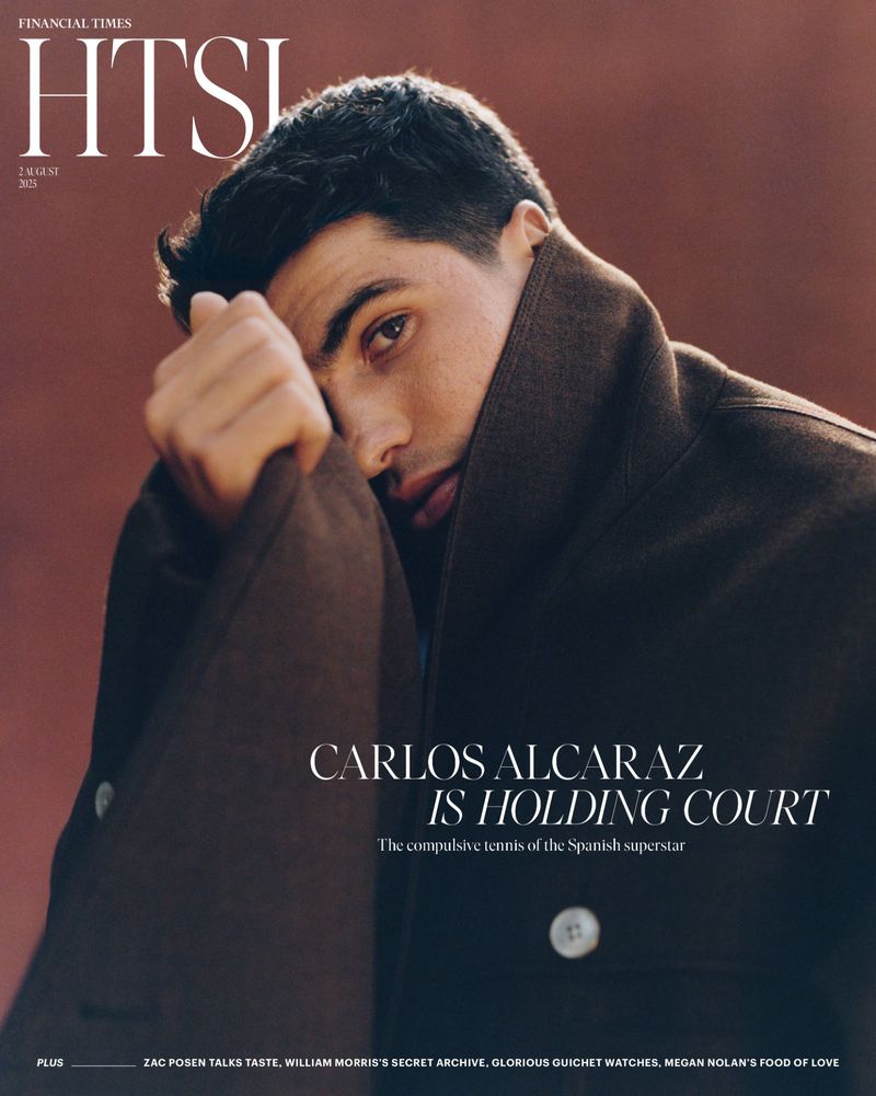 Portrait of Carlos Alcaraz on a magazine cover. He is looking toward the camera, with a hand at his face, wearing a brown coat. 