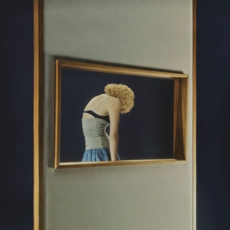 Artistic rendering of a fair-skinned woman with curly blonde hair, facing away, wearing a gray tank top and blue skirt, framed within an art frame.