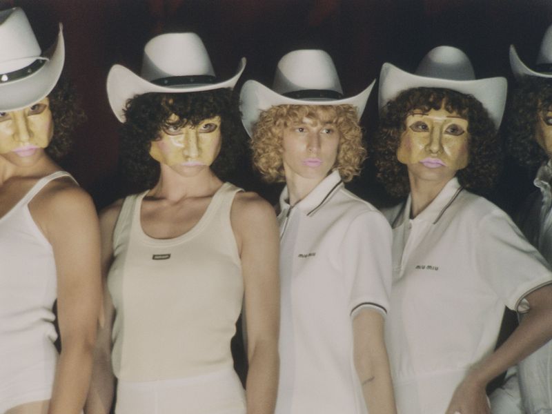 Group of people in matching white outfits and cowboy hats standing in front of a dark background. Fashion shoot, studio lighting.