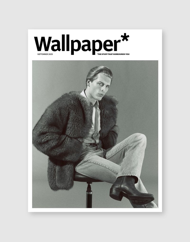 Wallpaper* magazine cover featuring a stylish man in a fur coat, light denim jeans, and black boots sitting in a studio setting.