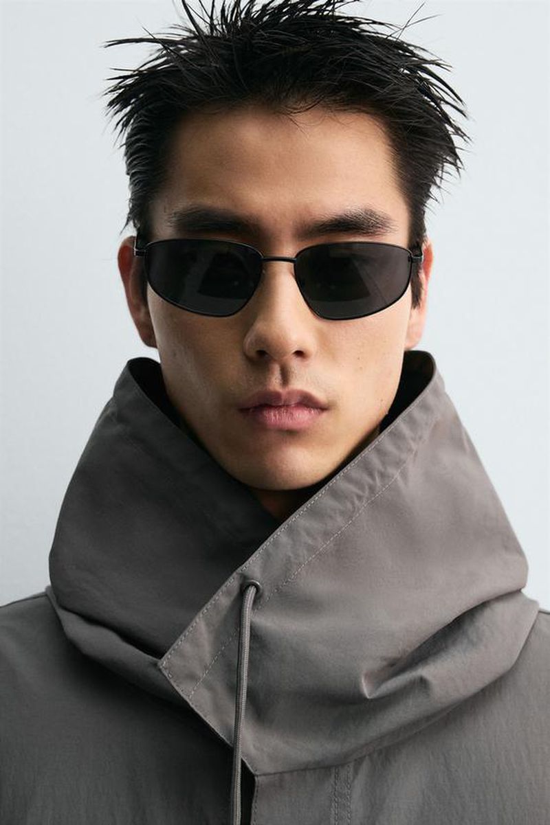 Asian man portrait wearing sunglasses and grey hooded raincoat in eye-level medium shot. Fashion promotion and product shot.