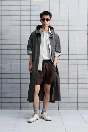 Model wearing a grey trench coat and dark sunglasses against a tiled wall backdrop for Zara
