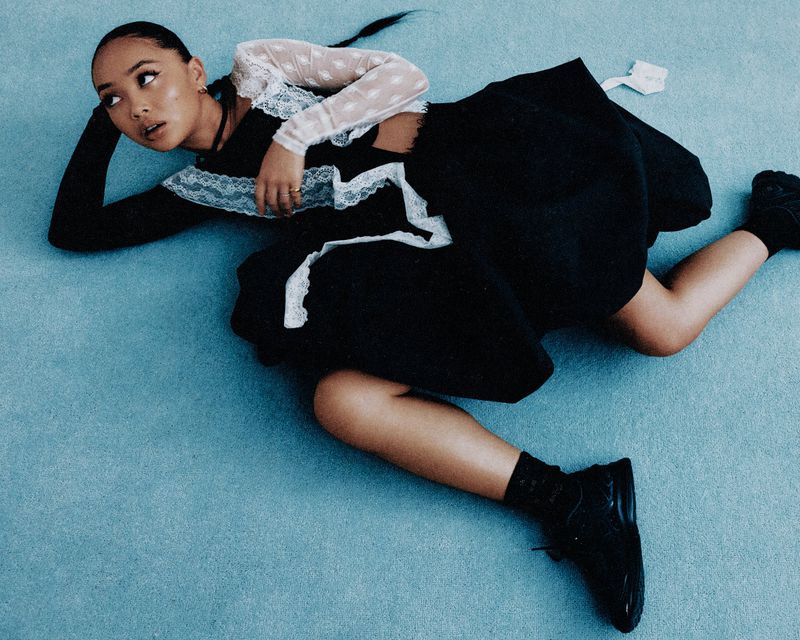 Fashion portrait of a young woman in a black dress with lace details lying on a light blue surface, high angle, studio lighting.