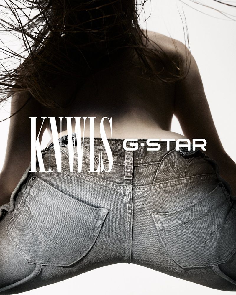 Back view of a slender person wearing jeans, showcasing the G-Star brand. Hair is tousled, with a bright, high-key lit background.
