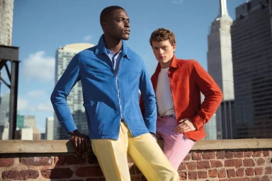 Two male models posing on a brick rooftop against an urban skyline for Paul Stuart Spring 2025.