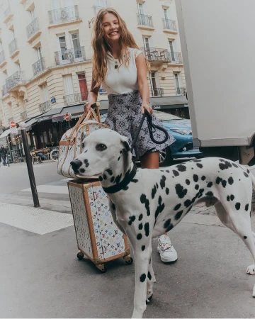 Smiling woman walking a Dalmatian on a city street, holding monogram luggage for Elle Australia
