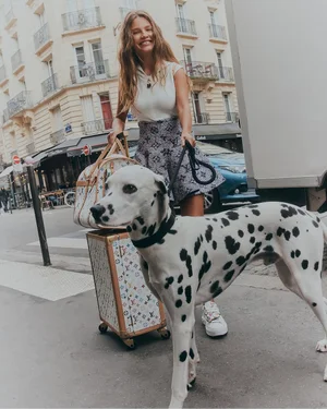 Smiling woman walking a Dalmatian on a city street, holding monogram luggage for Elle Australia