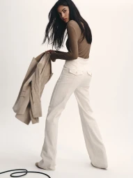 Model Rania Benchegra holding a beige blazer and wearing white trousers for Veronica Beard