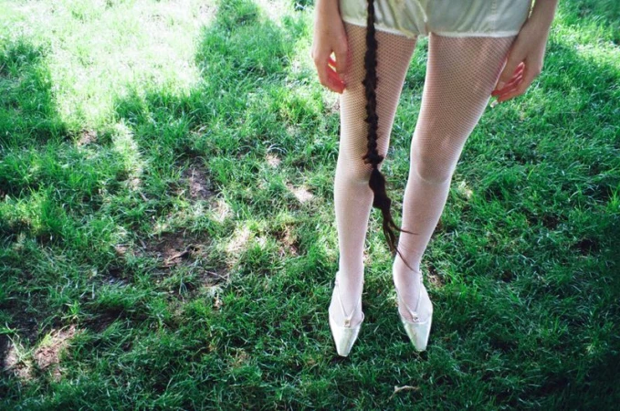 Person wearing tights and heels stands on green grass with hair braid visible. Outdoor setting with natural light in a close-up shot.