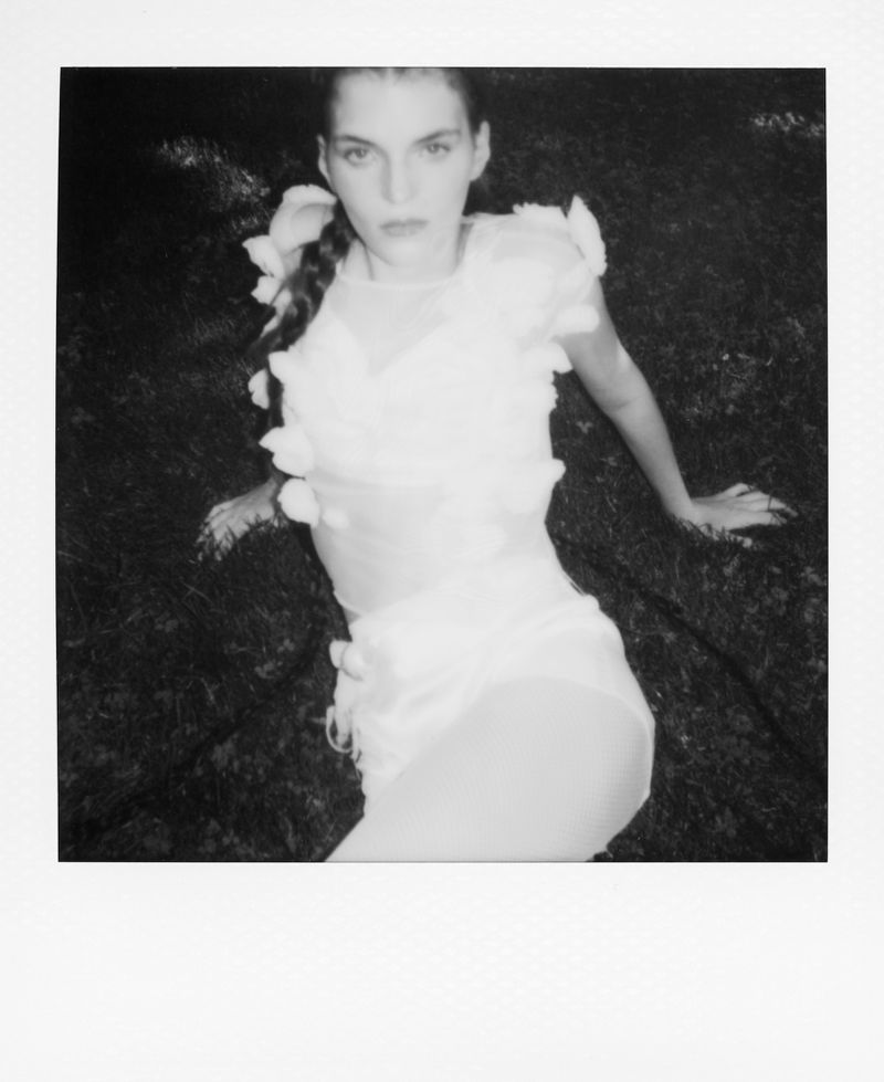 Monochrome image of a woman in light colored clothing lying in the grass, flowers are visible in her hair and on her outfit.