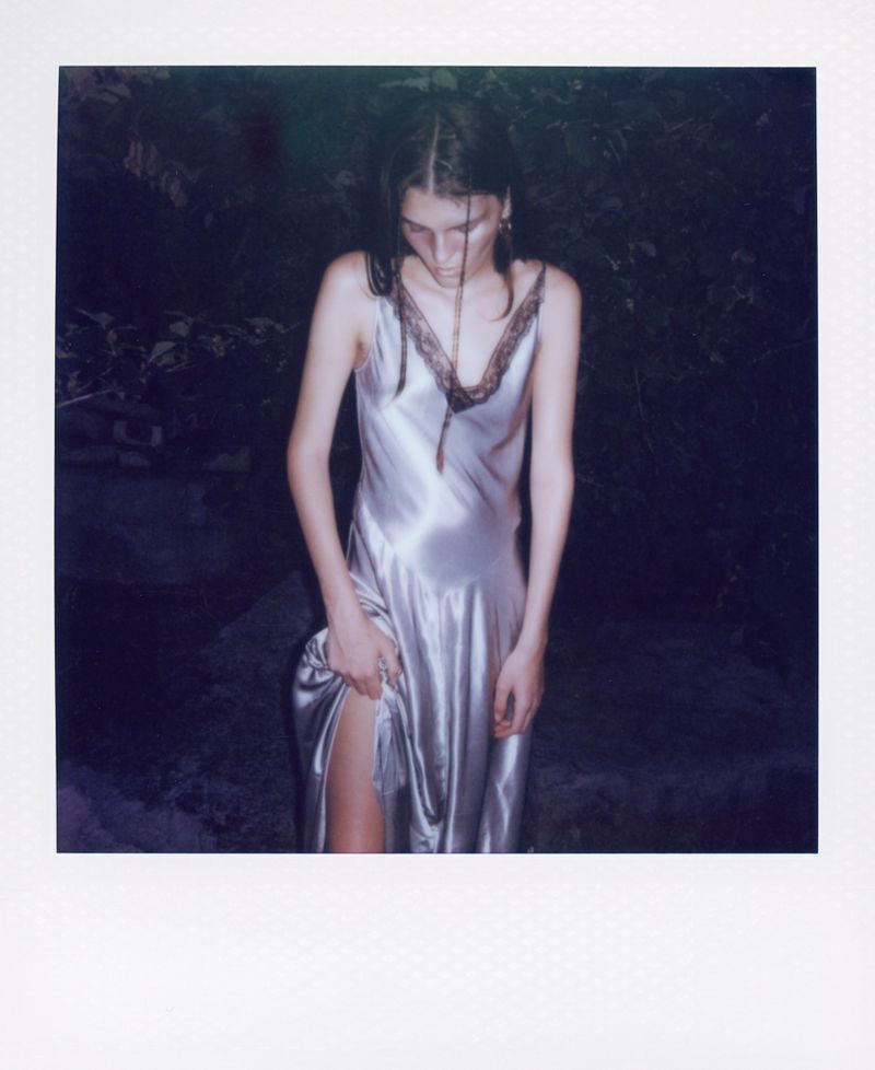 Woman in a silver dress with lace trim posing in a dark outdoor setting, with a polaroid border framing the photograph.