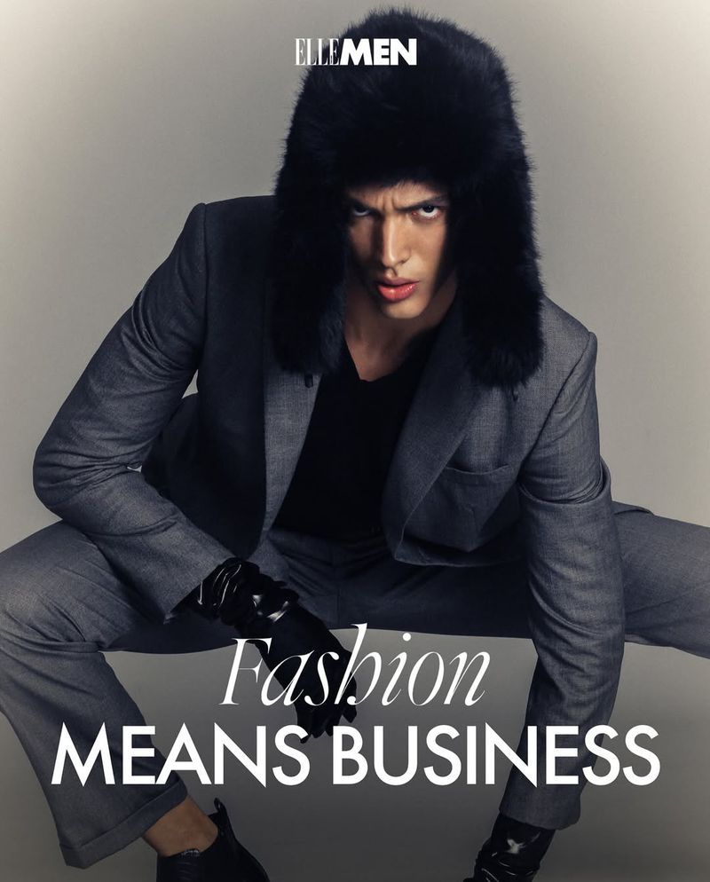 Man in a grey suit and fur hat poses for Elle Men fashion editorial, emphasizing sleek style against a neutral backdrop.