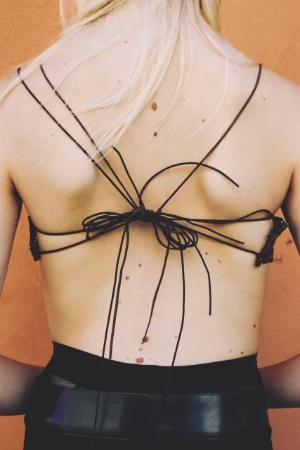 Back view of a fair-skinned female with blonde hair, wearing a black string top tied in the middle, and a black leather skirt with a belt.