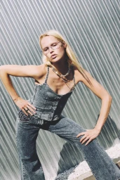 Blonde female model wearing acid wash denim corset top and matching jeans posing against corrugated metal wall