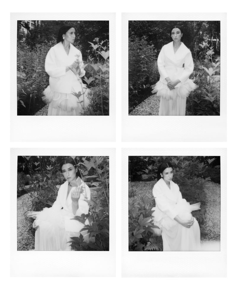 Four black and white instant photos of a woman in an outdoor setting, dressed in a light-colored dress and coat, surrounded by plants.