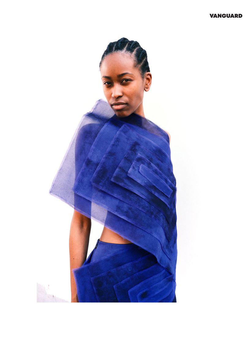 Fashion shot of a Black female model wearing a royal blue textured top and skirt in a bright photo studio with Vanguard text.